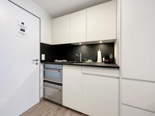 a kitchen with white cabinets and a black wall at Phoenix Studio - Haus Astral - Zermatt in Zermatt