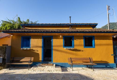 ein gelbes Gebäude mit zwei Bänken davor in der Unterkunft Casa aconchegante no coração do Bairro do Quilombo in São Bento do Sapucaí