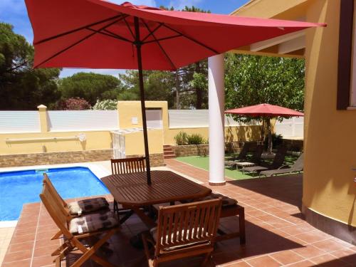 a patio table with a red umbrella next to a pool at Playa Eucaliptos 1A in Isla Cristina