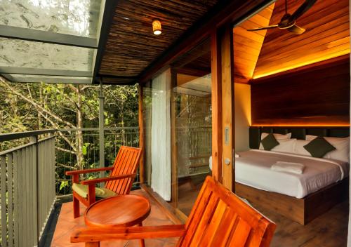 Zimmer mit einem Bett und zwei Stühlen auf einer Veranda in der Unterkunft Chembarathi Wayanad Boutique Resort in Vaduvanchal