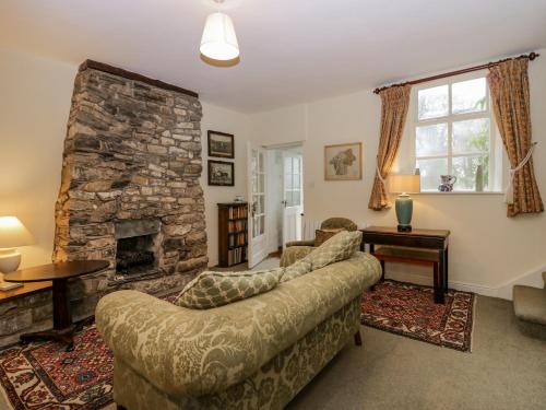 a living room with a couch and a stone fireplace at Longlands Groom's Quarters in Cartmel