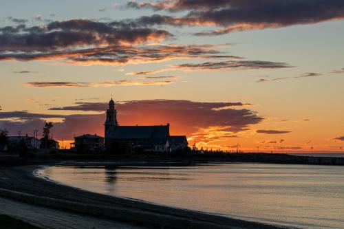 a sunset over the water with a building and a clock tower at Navigateur Ste-Luce in Sainte-Luce-sur-Mer