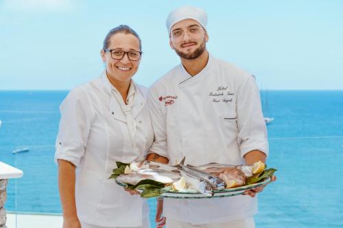 Un uomo e una donna che tengono in mano un piatto di pesce di Hotel Ferdinando Beach & Thermal Spa a Ischia