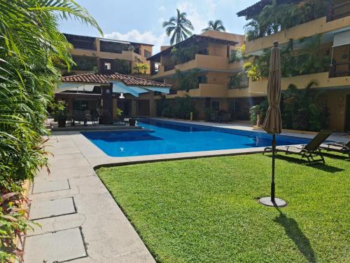a swimming pool in front of a building with an umbrella at " Los Mangos" 2 bedroom 2 Bathroom appartment at walking distance from the beach in Zihuatanejo