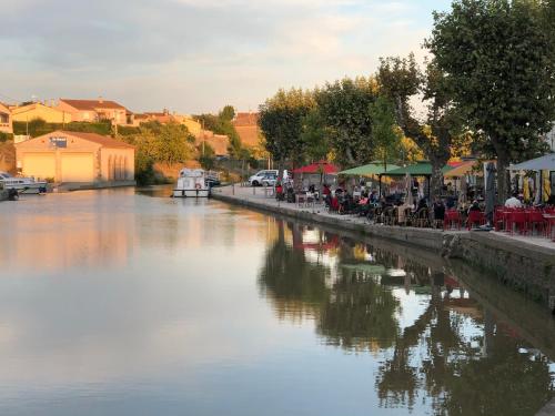 a river with a group of people sitting at tables by the water at Le Petit Relais du Canal in Trèbes