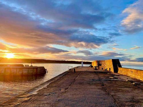 a pier with the sun setting over the water at Hill Crest - cliff top cottage with stunning views in Cullen