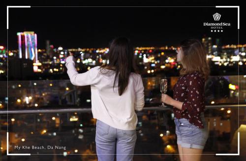 two women standing on a ledge with a glass of wine at Diamond Sea Hotel in Da Nang