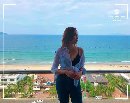 a woman standing on a balcony looking at the beach at Diamond Sea Hotel in Da Nang