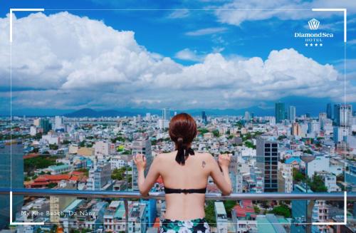 a woman in a bikini standing on a balcony overlooking a city at Diamond Sea Hotel in Da Nang