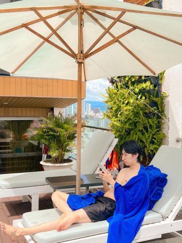 a man in a blue dress sitting on a chair under an umbrella at Diamond Sea Hotel in Da Nang