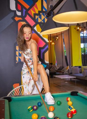 a young girl sitting on a pool table with a cue at Cassia Phuket, part of Banyan Group in Bang Tao Beach