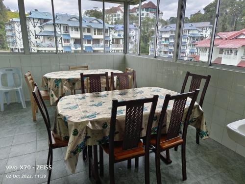 ein Esszimmer mit 2 Tischen, Stühlen und Fenstern in der Unterkunft Bani's Penthouse (Homestay Cameron Highlands) in Tanah Rata