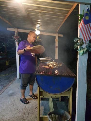 a man is cooking food on a grill at Tmn Rekreasi Cikgu Haron in Labis