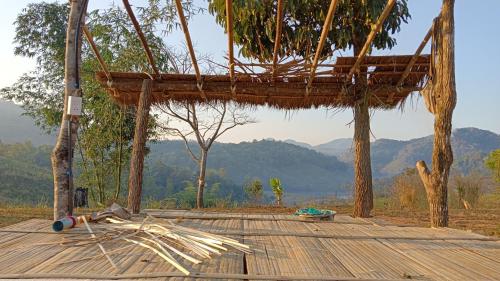 a wooden deck with a thatched roof with mountains in the background at ไร่นิธิสุนทร nithisoonthon farmstay in Mae Hong Son
