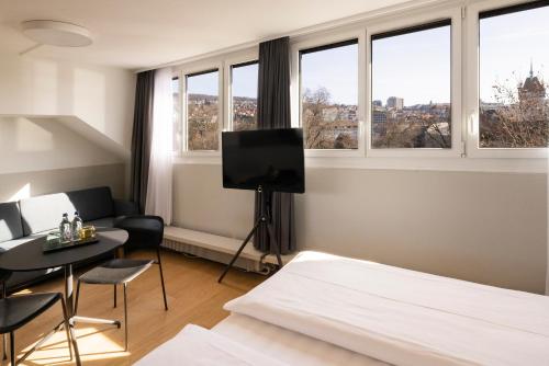 a bedroom with a bed and a tv and windows at Fred Hotel Zürich Hauptbahnhof in Zurich