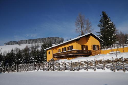 a yellow house in the snow next to a fence at Sulamith Ferienhaus mit Garten in Sankt Kathrein am Offenegg