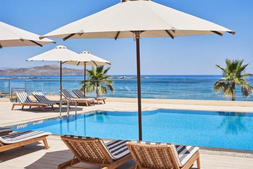 a swimming pool with chairs and umbrellas and the ocean at Atlantica Kalliston Resort - Adults Only in Stalos