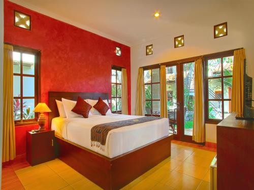 a bedroom with a bed with red walls and windows at Puri Sading Hotel in Sanur