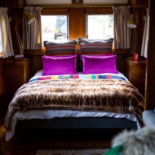 Showman's Caravan في بانشوري: غرفة نوم مع سرير مع وسائد أرجوانية