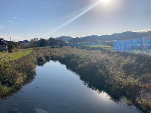 a river in a field with the sun in the sky at FARMSTAY miyuki-street "Goen" in Ukiha