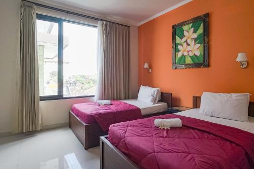 two beds in a room with orange walls and a window at Taxa Uma Guest House in Kuta