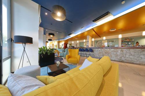 a lobby with a yellow couch and a bar at Hotel Ilirija in Biograd na Moru