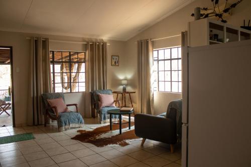 een woonkamer met stoelen en een tafel en ramen bij Hello Kruger Hideaway Cottage & Skilpad Studio in Marloth Park