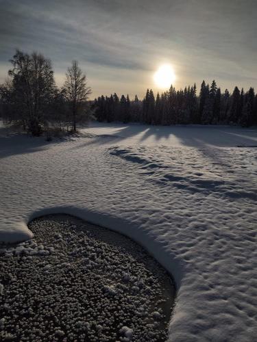 a river in the snow with the sun in the background at Lugnet Malung Hotell in Malung