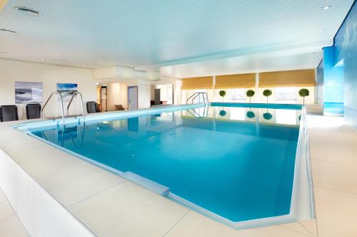 a large swimming pool with blue water in a room at Best Western Plus Arosa Hotel in Paderborn