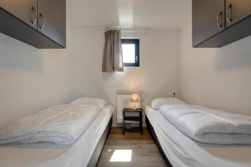 two beds in a room with a table and a window at Recreatiepark Jachthaven De Veerstal Lathum - Luxe Chalet in Lathum