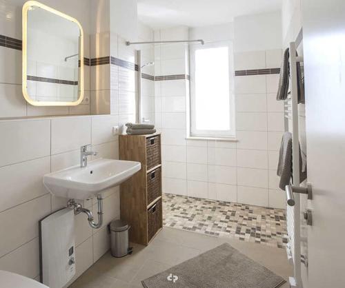 een witte badkamer met een wastafel en een spiegel bij DUENENZEIT App Nr 5 max 4 Pers in Dierhagen