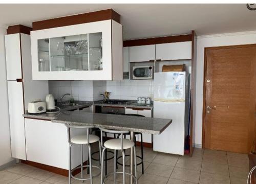 a kitchen with white cabinets and a counter with bar stools at Departamentos Costa Pingueral in Tomé