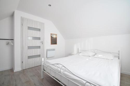 a white bedroom with a white bed and a door at Domki Wierzbówka in Mielno