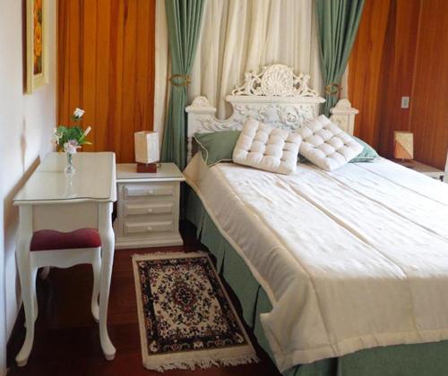 a bedroom with a white bed with a table and a drawer at Pousada Casa dos Sonhos in Campos do Jordão