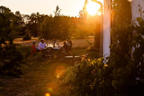 Klippinge的住宿－The Norrmans Farmhouse Boutique Hotel，一群人坐在花园的桌子上,日落时分