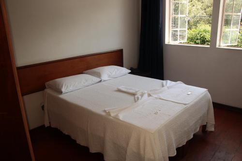 een slaapkamer met een bed met witte lakens en een raam bij Pousada Villa Real in Sabará