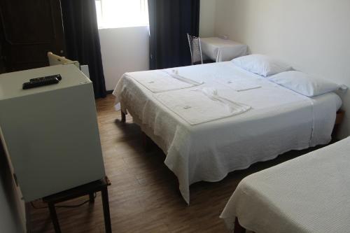 a bedroom with a white bed and a dresser and a table at Pousada Villa Real in Sabará