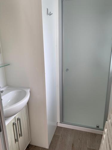 La salle de bains est pourvue d'un lavabo et d'une porte de douche en verre. dans l'établissement Location Mobilhome, à Narbonne-Plage