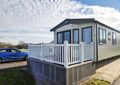 a small house with a white fence and a blue car at Perran Heights Holiday Park in Perranzabuloe