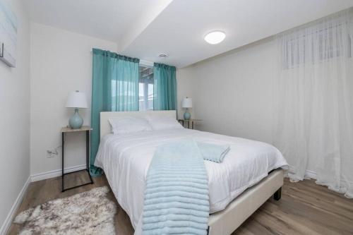 ein weißes Schlafzimmer mit einem großen Bett und einer blauen Decke in der Unterkunft *Modern & Cozy* Basement 1 Bdrm W/Fast Internet & Smart TV in Barrie