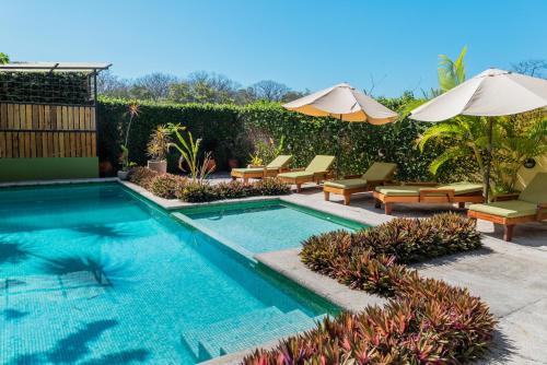 a swimming pool with chairs and umbrellas in a yard at Nautilus Surf & Yoga Villas Santa Teresa in Santa Teresa Beach