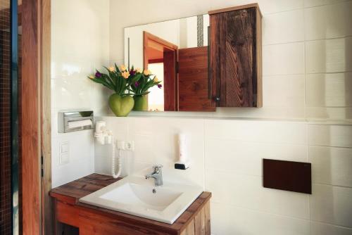 a bathroom sink with a mirror and a vase of flowers at Gasthaus Georg Ludwig Maising in Pöcking