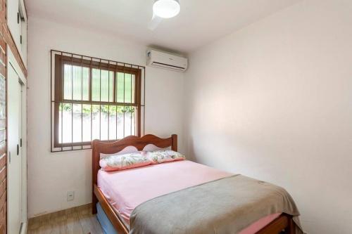 Schlafzimmer mit einem Bett mit rosa Bettwäsche und einem Fenster in der Unterkunft CASA CORAL SAQUAREMA in Saquarema