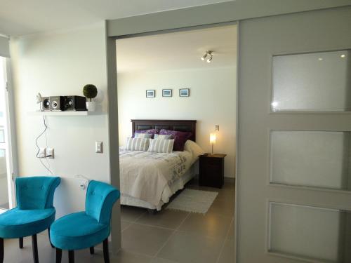 a bedroom with a bed and two blue chairs at Laguna del Mar Suites in La Serena