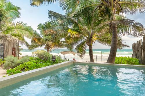 una piscina frente a una playa con palmeras en Casa Ganesh Tulum, en Tulum