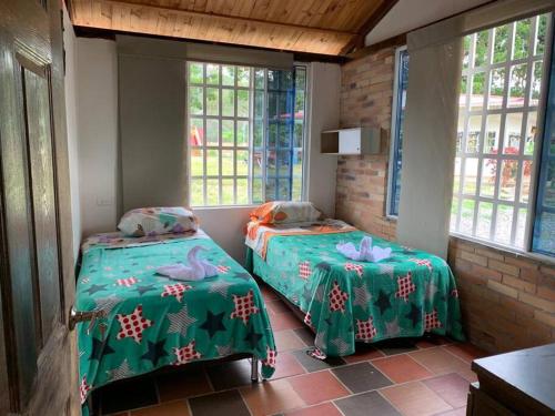 Habitación con 2 camas, sábanas verdes y ventanas. en Casa de campo ideal para descanso, en Villavicencio