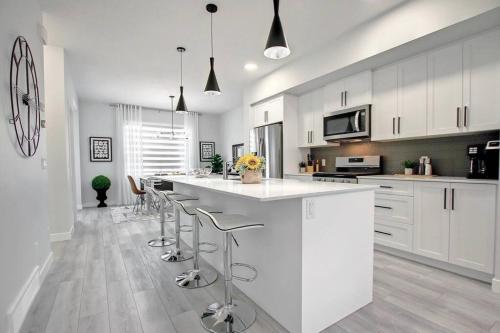 a kitchen with white cabinets and a large island with bar stools at Beautiful 3Bed-with AC-Close to Spruce Meadows & Mountains in Calgary
