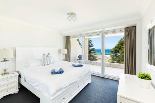 a white bedroom with a large bed and a large window at Luxury Manly Beachfront Apartment in Sydney