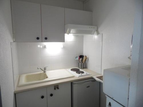 La cuisine blanche est équipée d'un évier et d'un réfrigérateur. dans l'établissement Appartement cosy à 200m de la plage avec parking privé et loggia, animaux admis - FR-1-326-668, à Marseillan