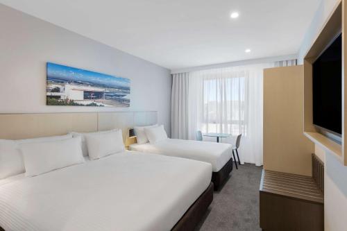 a hotel room with two beds and a flat screen tv at Travelodge Hotel Sydney Airport in Sydney